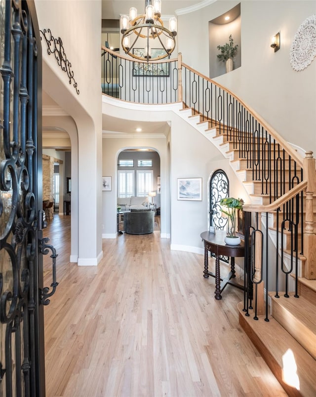 foyer entrance featuring an inviting chandelier, wood finished floors, arched walkways, and ornamental molding