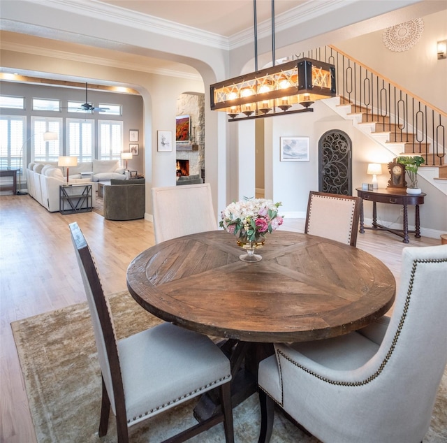 dining room with wood finished floors, stairway, arched walkways, a lit fireplace, and crown molding