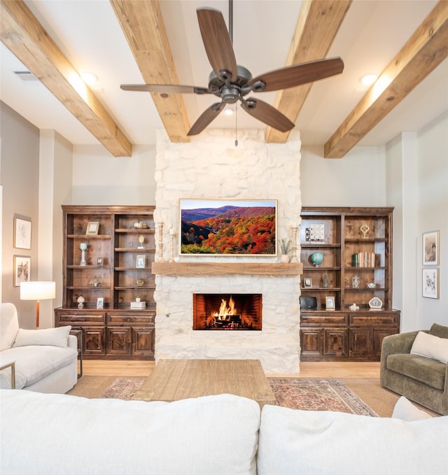 living room featuring a stone fireplace, beamed ceiling, and ceiling fan