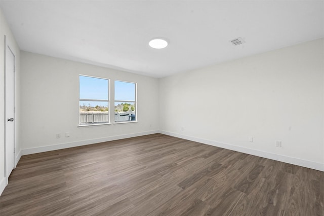 empty room featuring dark wood finished floors, visible vents, and baseboards