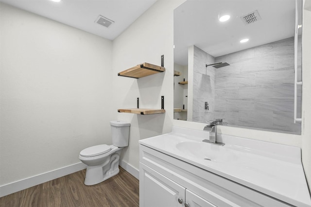 bathroom with vanity, wood finished floors, visible vents, tiled shower, and toilet