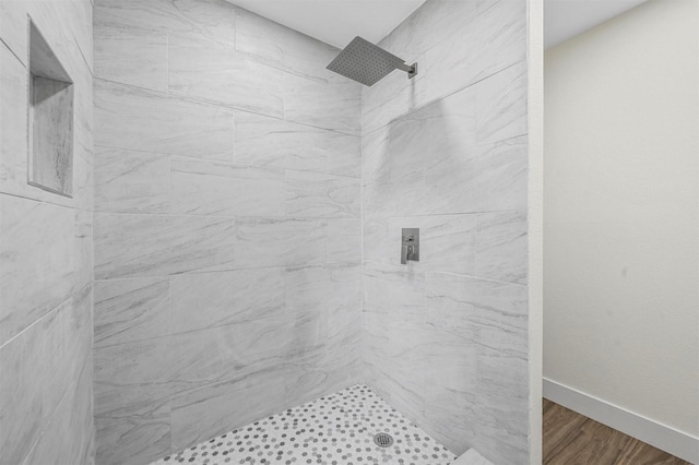 full bath featuring a tile shower, baseboards, and wood finished floors