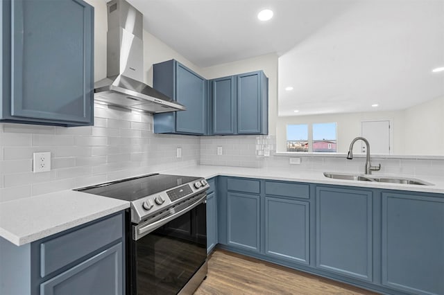 kitchen with electric range, blue cabinetry, wall chimney exhaust hood, and a sink