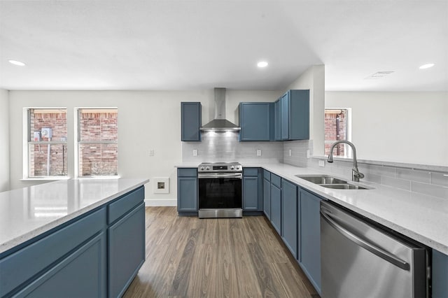 kitchen with a sink, tasteful backsplash, dark wood finished floors, appliances with stainless steel finishes, and wall chimney exhaust hood