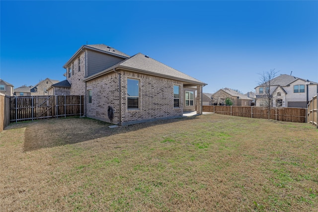 rear view of house featuring a lawn, brick siding, a fenced backyard, and roof with shingles