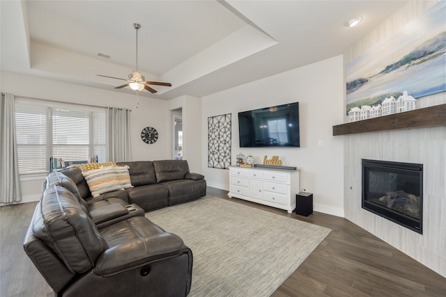 living area featuring a fireplace, a raised ceiling, baseboards, and wood finished floors