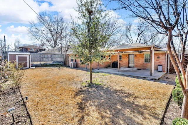 back of house featuring brick siding, cooling unit, a fenced backyard, an outbuilding, and a patio