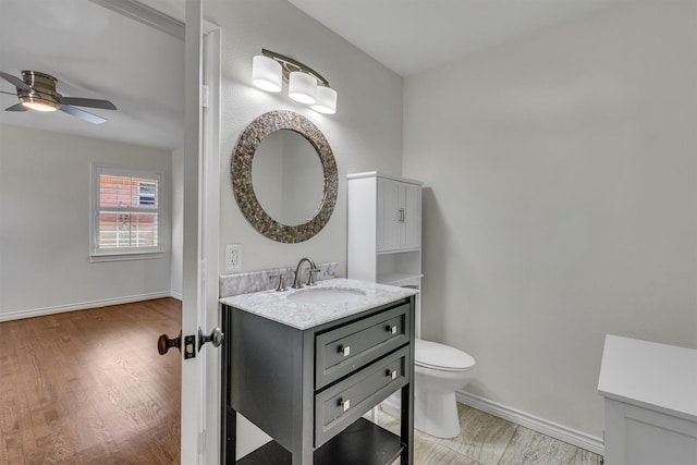 bathroom featuring vanity, wood finished floors, baseboards, ceiling fan, and toilet