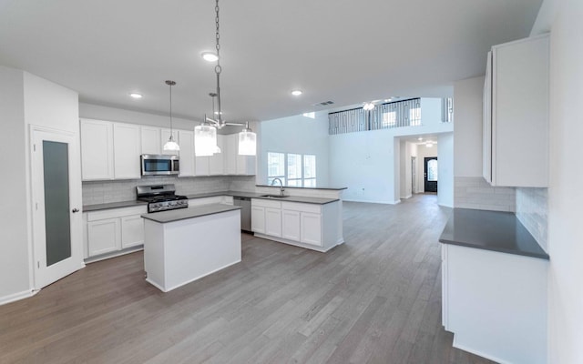 kitchen with light wood finished floors, a sink, stainless steel appliances, white cabinetry, and a center island