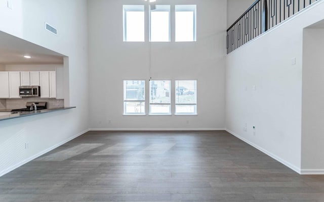 unfurnished living room with visible vents, baseboards, a high ceiling, and wood finished floors