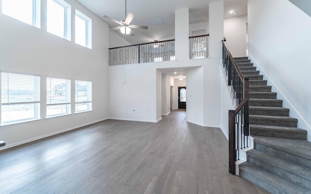 unfurnished living room with visible vents, baseboards, ceiling fan, stairway, and wood finished floors