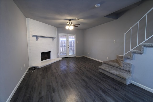 unfurnished living room featuring a brick fireplace, stairs, baseboards, and wood finished floors