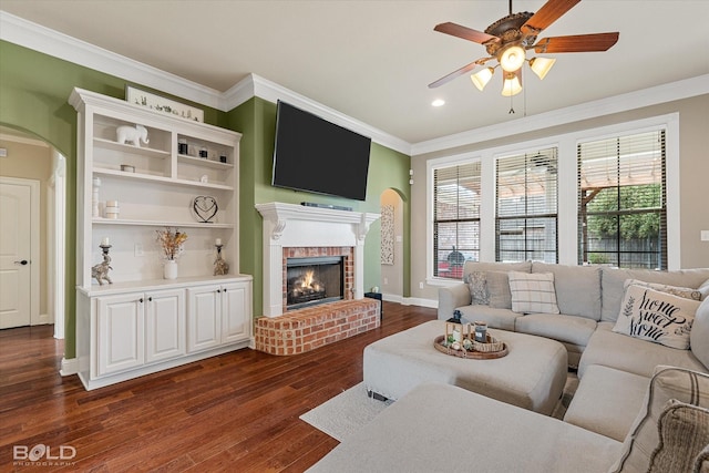 living room featuring a wealth of natural light, arched walkways, a brick fireplace, and ornamental molding