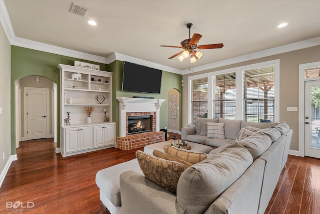 living area featuring arched walkways, visible vents, a brick fireplace, and ornamental molding