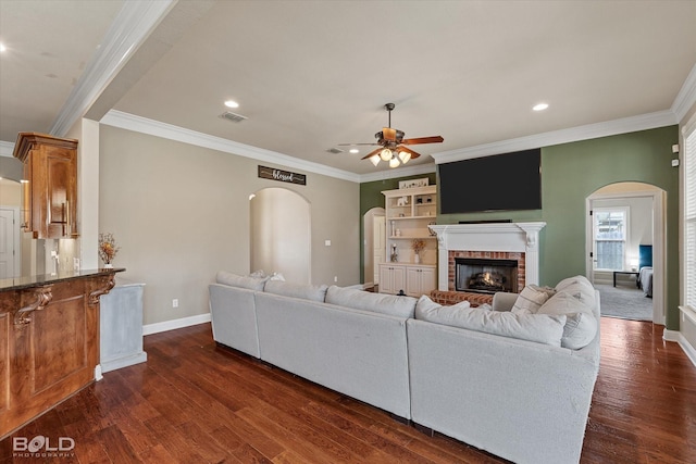 living area featuring a ceiling fan, baseboards, visible vents, dark wood finished floors, and a brick fireplace