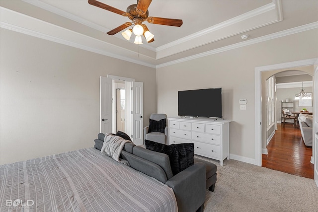 bedroom featuring a raised ceiling, ceiling fan with notable chandelier, arched walkways, crown molding, and baseboards