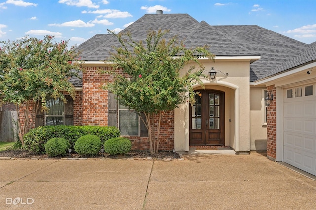 entrance to property with stucco siding, driveway, a shingled roof, a garage, and brick siding