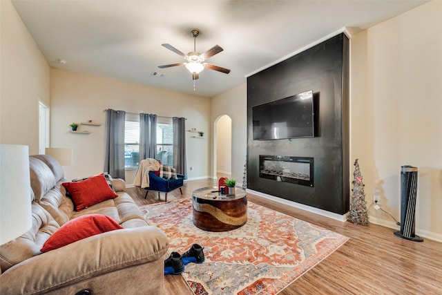 living room featuring wood finished floors, baseboards, visible vents, arched walkways, and a large fireplace