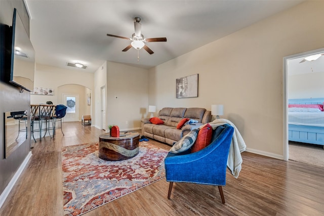 living room featuring baseboards, arched walkways, wood finished floors, and a ceiling fan