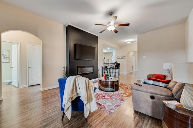 living room with a ceiling fan, wood finished floors, arched walkways, and a large fireplace