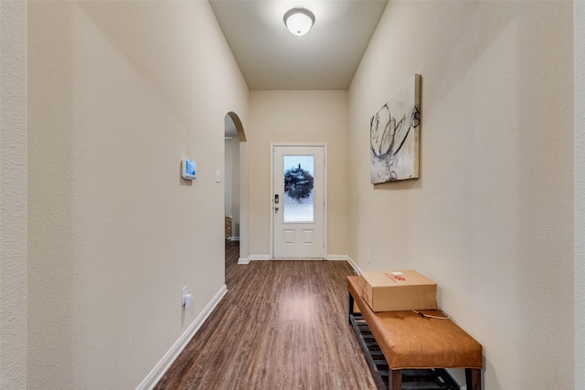 doorway to outside featuring dark wood-type flooring, baseboards, and arched walkways