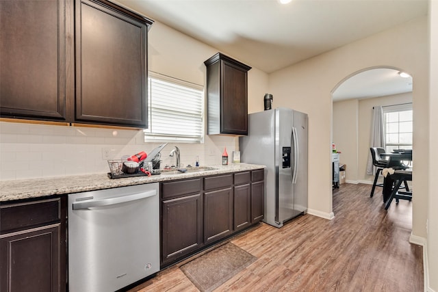 kitchen featuring dark brown cabinets, decorative backsplash, light wood-style flooring, appliances with stainless steel finishes, and arched walkways