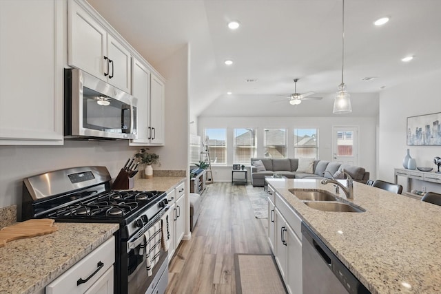 kitchen featuring light wood-type flooring, a sink, open floor plan, appliances with stainless steel finishes, and white cabinets