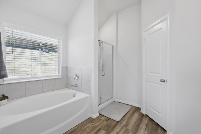 bathroom featuring wood finished floors, baseboards, lofted ceiling, a shower stall, and a garden tub