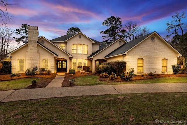 view of front of home with a yard, french doors, brick siding, and a chimney