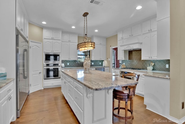 kitchen featuring visible vents, a kitchen island, built in appliances, light wood-type flooring, and white cabinets