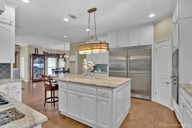 kitchen with visible vents, a kitchen island, light wood finished floors, decorative backsplash, and built in appliances