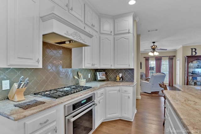 kitchen with visible vents, custom range hood, appliances with stainless steel finishes, light wood-style floors, and white cabinets