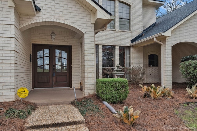 property entrance featuring french doors, brick siding, and a shingled roof