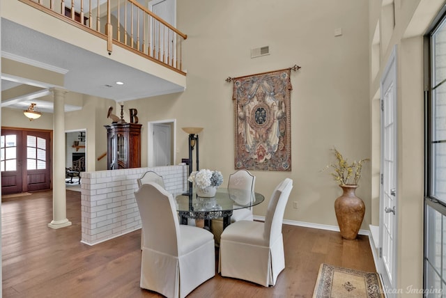 dining room with wood finished floors, visible vents, ornate columns, baseboards, and a high ceiling