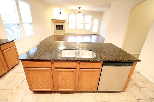 kitchen featuring open floor plan, a center island with sink, dishwasher, a fireplace, and a sink