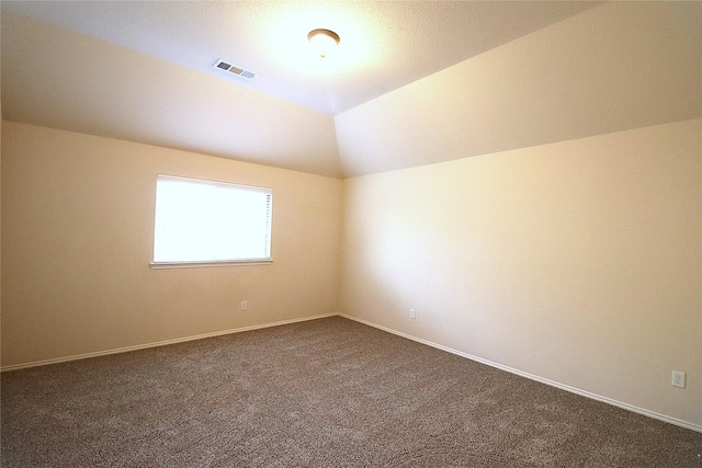 unfurnished room featuring visible vents, dark carpet, baseboards, and lofted ceiling