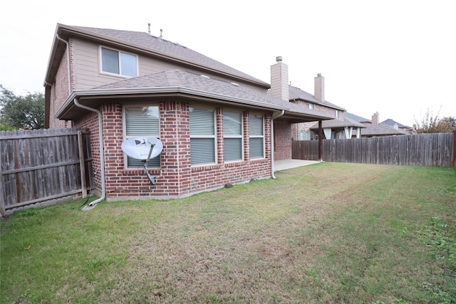 back of property with brick siding, a fenced backyard, and a yard