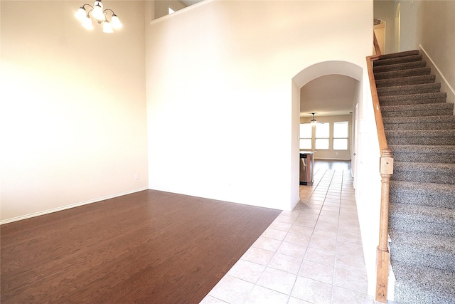 empty room with a high ceiling, light tile patterned flooring, arched walkways, stairs, and a chandelier