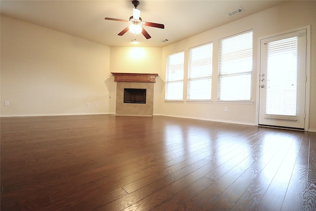 unfurnished living room with dark wood-style floors, visible vents, a tiled fireplace, and baseboards