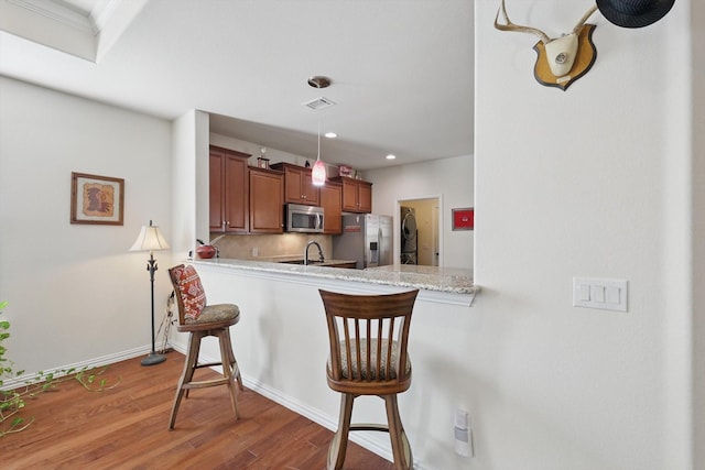 kitchen featuring visible vents, tasteful backsplash, wood finished floors, appliances with stainless steel finishes, and a breakfast bar area