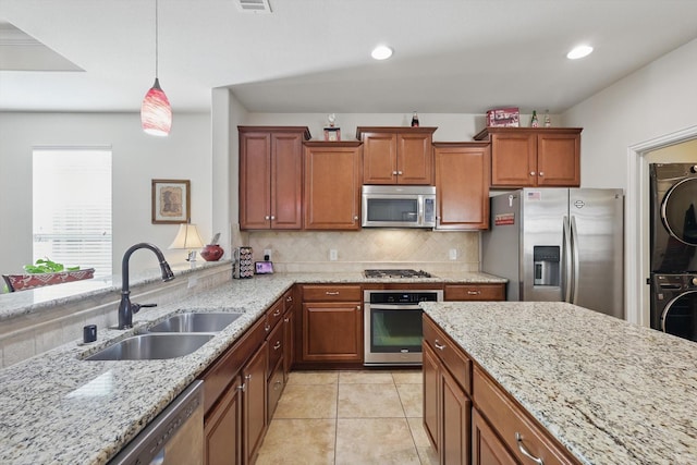 kitchen featuring light stone countertops, stacked washer and dryer, decorative backsplash, stainless steel appliances, and a sink