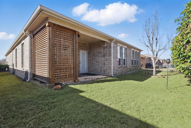 view of property exterior featuring fence, a lawn, and brick siding