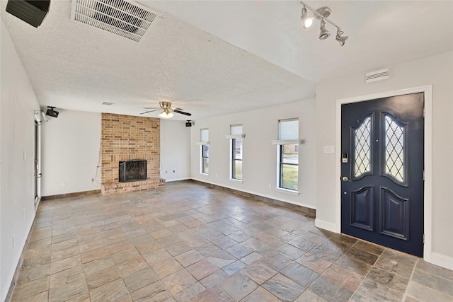 foyer entrance with baseboards, visible vents, ceiling fan, a textured ceiling, and a brick fireplace