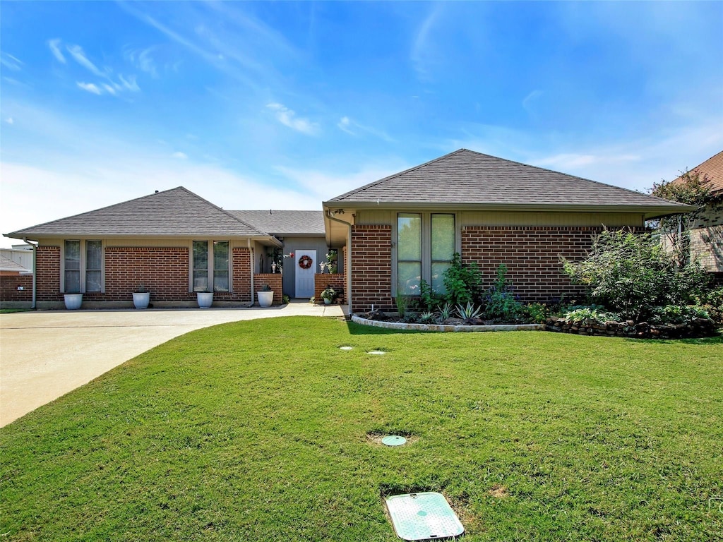 single story home featuring brick siding, a front lawn, driveway, and a shingled roof