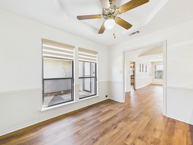 empty room with a ceiling fan, wood finished floors, visible vents, and baseboards