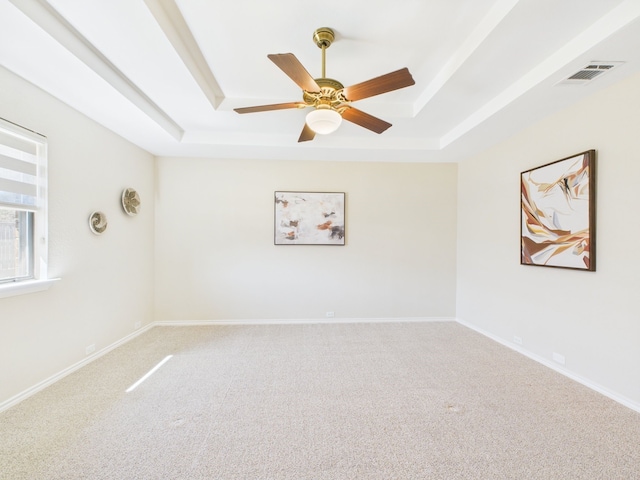 carpeted empty room with a tray ceiling, baseboards, visible vents, and ceiling fan