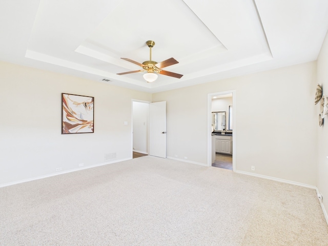 empty room featuring visible vents, carpet, a raised ceiling, and baseboards