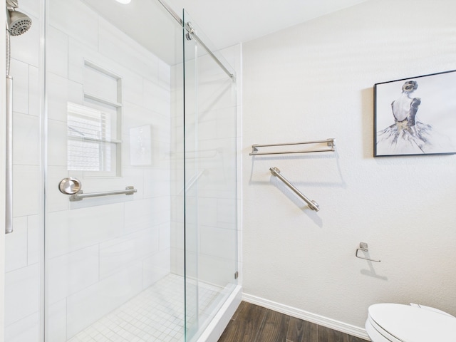 bathroom with baseboards, wood finished floors, toilet, and a stall shower