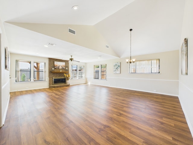 unfurnished living room featuring ceiling fan with notable chandelier, a brick fireplace, wood finished floors, and visible vents