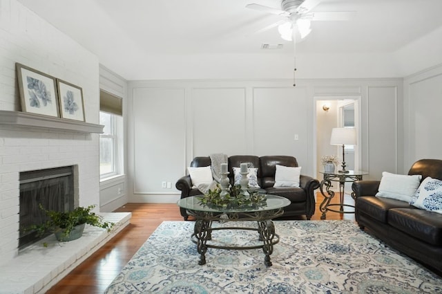 living room featuring visible vents, ceiling fan, dark wood finished floors, a fireplace, and a decorative wall